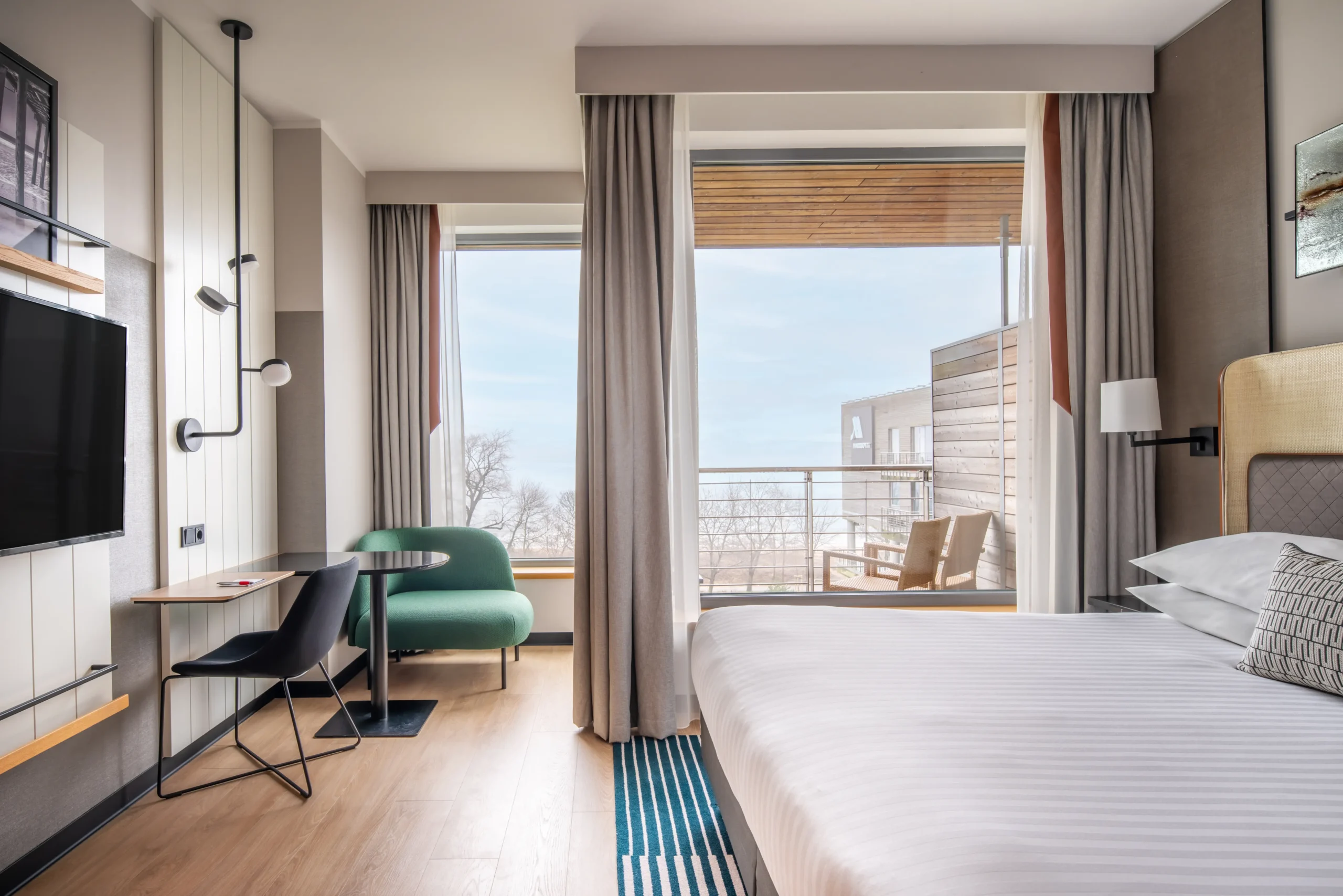 Zrealizowany fit-out hotelowego pokoju z łóżkiem, biurkiem, zieloną sofą i balkonem