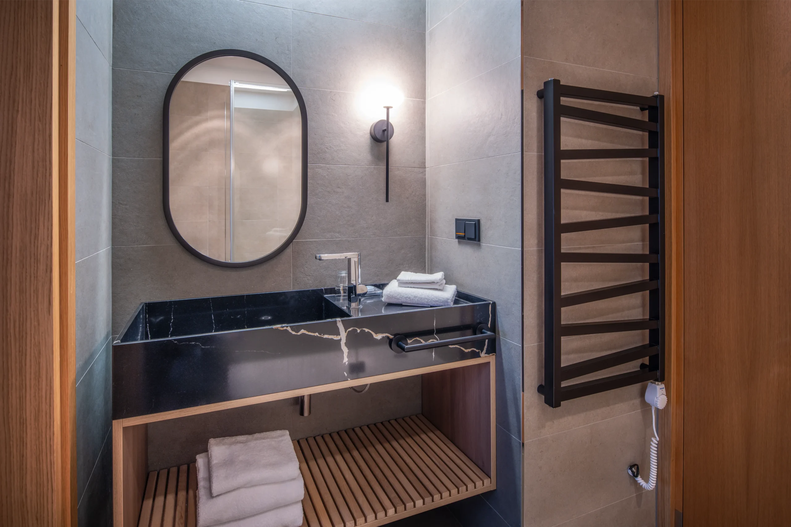 Aranżacja łazienki: nowoczesna łazienka z czarną marmurową umywalką, owalnym lustrem i drewnianą półką