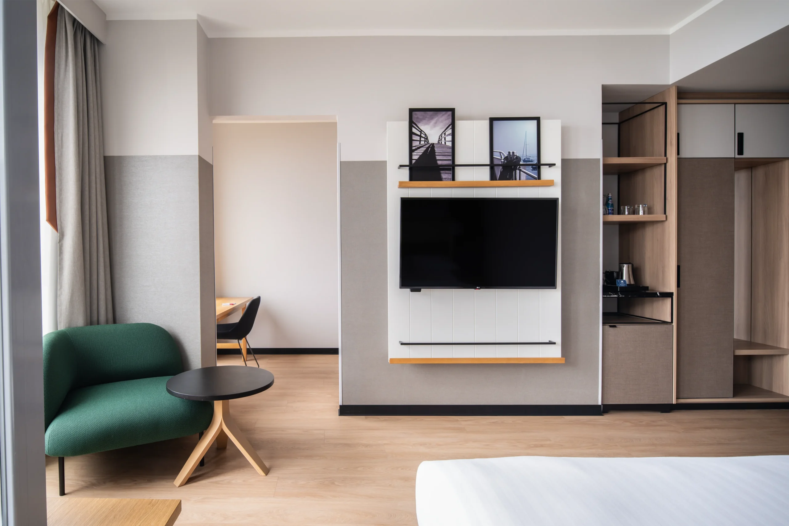 Nowoczesny pokój hotelowy z drewnianą podłogą, szafą, telewizorem, zielonym fotelem i biurkiem – Wykończenie wnętrz