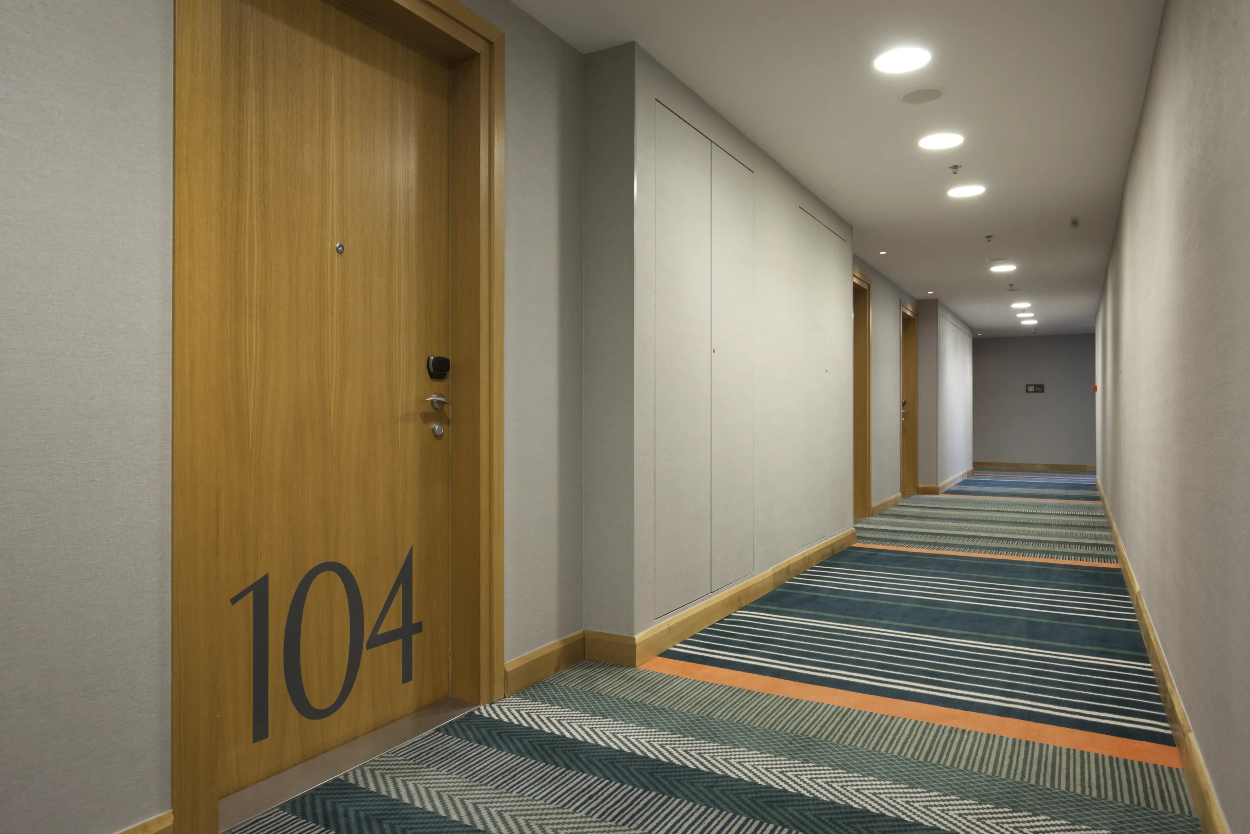Kompleksowy korytarz hotelowy z drewnianymi drzwiami pokoju 104 i oświetleniem sufitowym – Fit-out