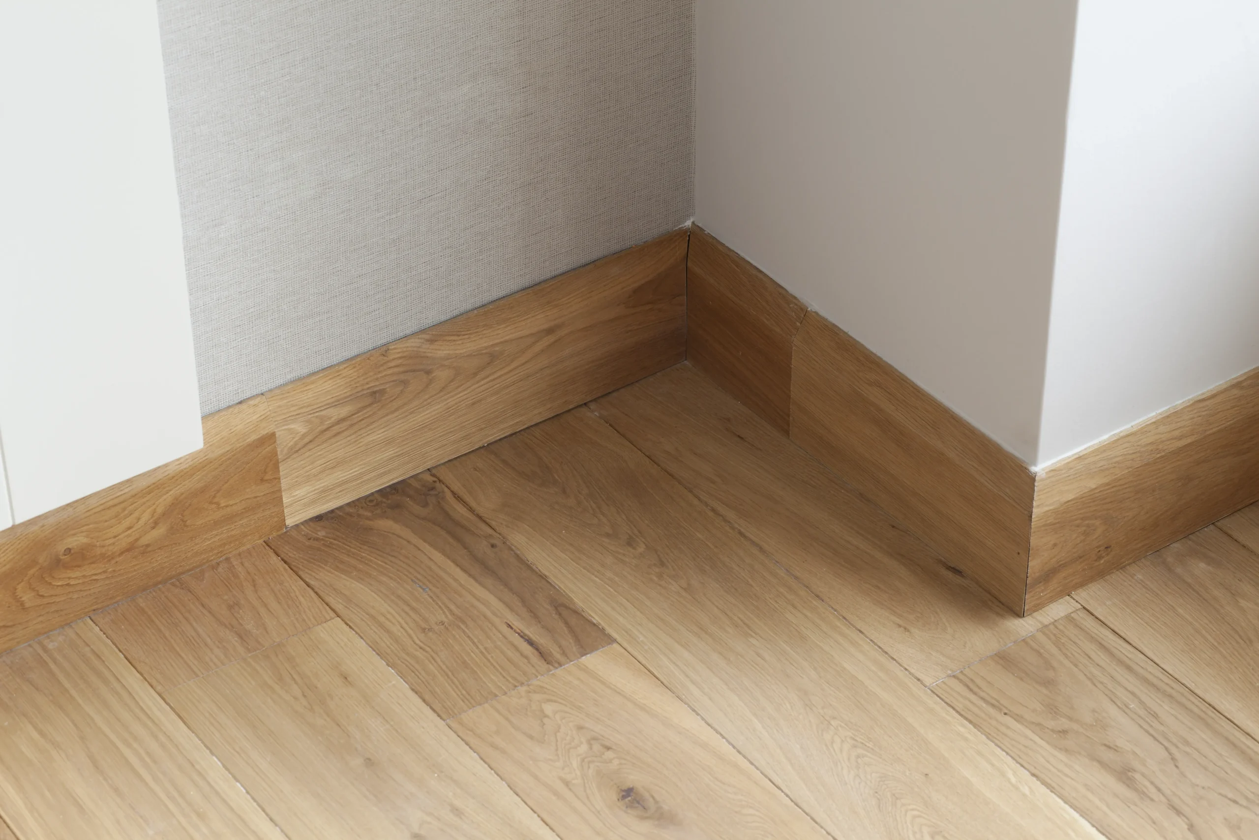 Kąt pomieszczenia z dębową podłogą warstwową i drewną listwą przypodłogową, przykład wykończenia wnętrz