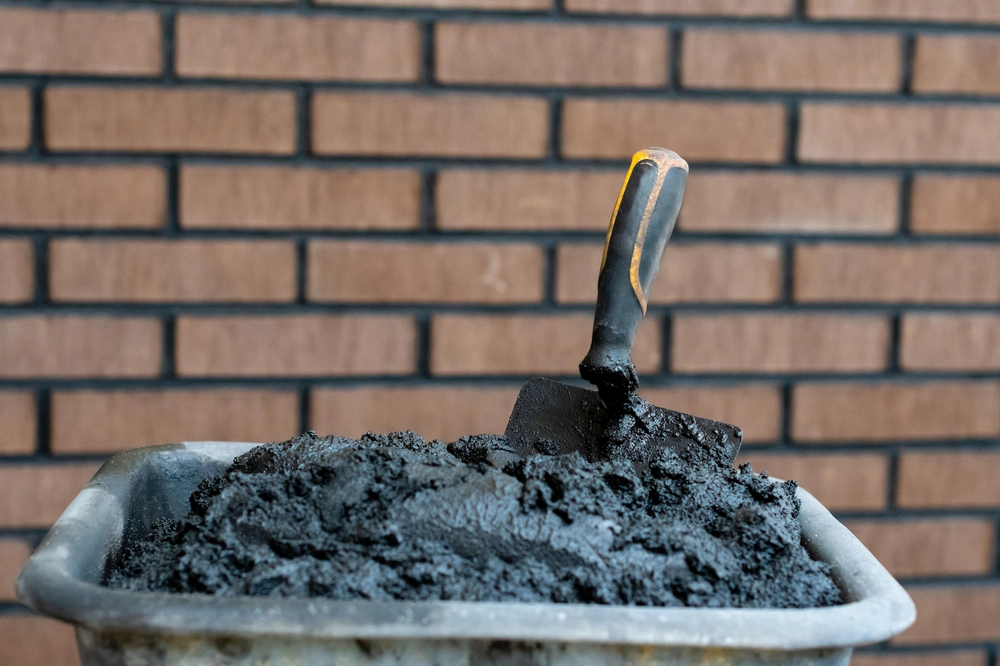 Zaprawa murarska w taczce z kielnią na tle ceglanej ściany, etap Murowanie