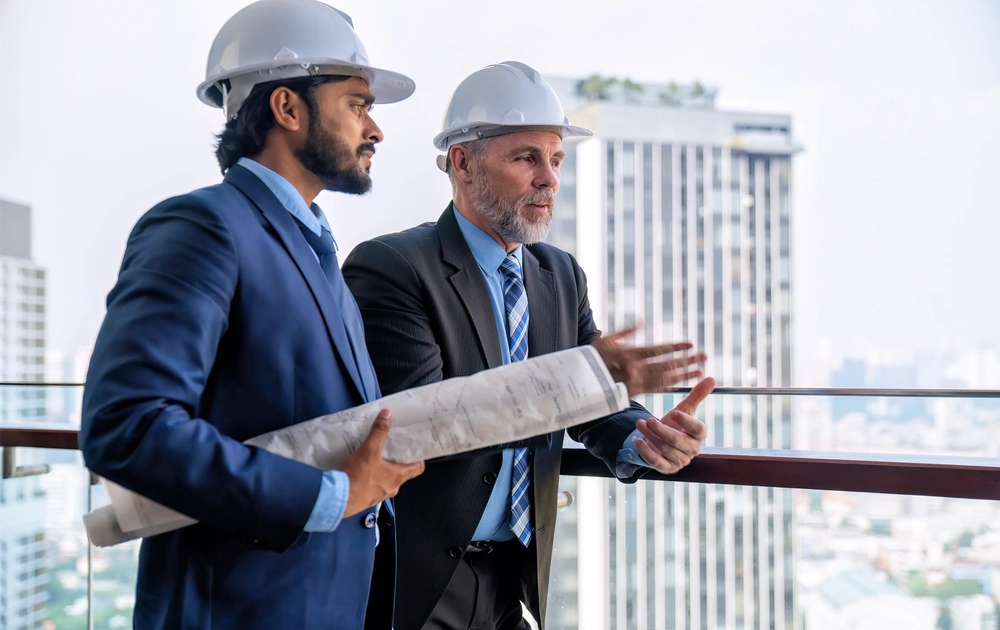Dwóch mężczyzn w kaskach przegląda plany na balkonie z widokiem na miasto, Inwestor zastępczy