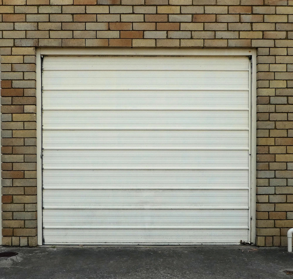 Zamknięta biała brama garażowa z poziomymi panelami osadzona w ceglanej ścianie – Bramy garażowe