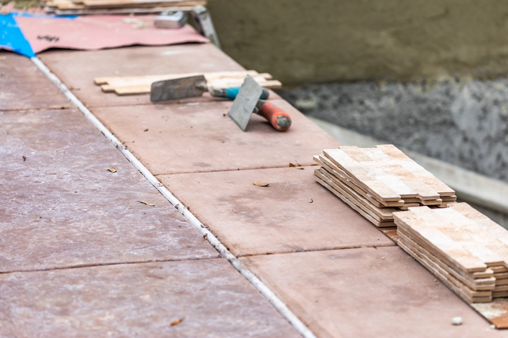 Fragment ułożonych bordowych płytek podłogowych, narzędzia i stos kolejnych elementów – usługa Układanie płytek