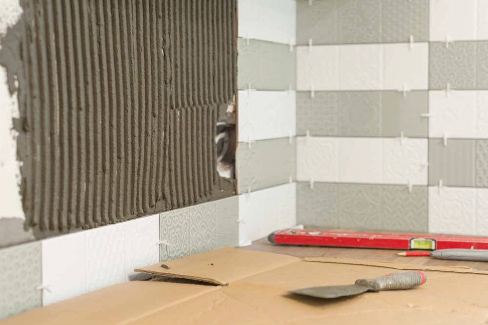 Układanie płytek na ścianie – biało-szare kafelki z krzyżykami układane przy użyciu kielni i poziomicy