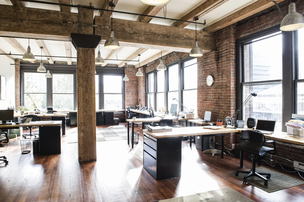 Jasne wnętrze biura pod klucz w stylu industrialnym z drewnianymi belkami, stalowymi lampami i przestrzennymi stanowiskami pracy