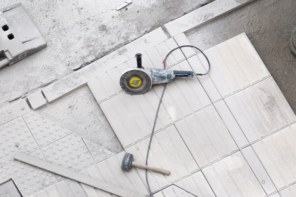 Szlifierka kątowa, gumowy młotek i prosto ułożone jasne płytki podczas układania płytek