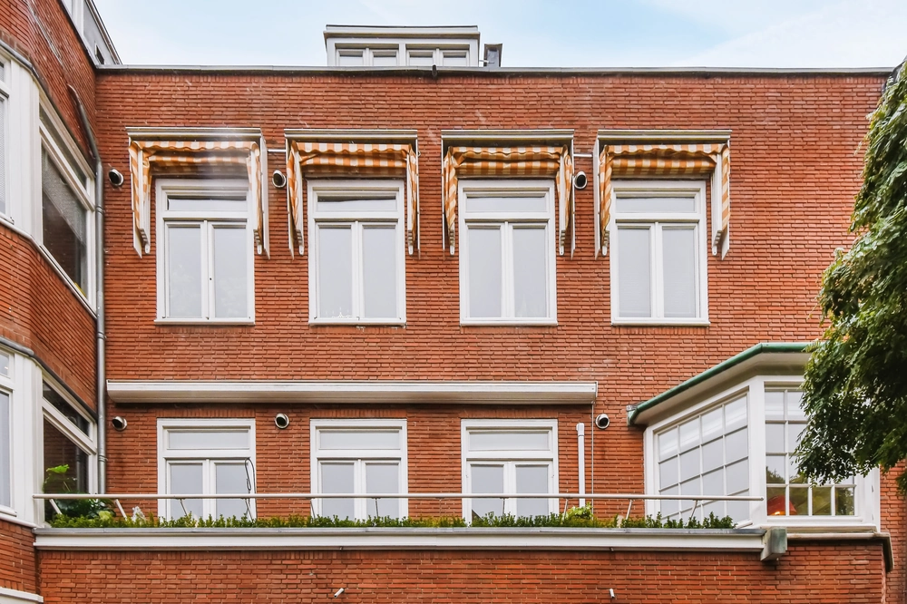 Elewacje budynku z czerwonej cegły z białymi oknami i pomarańczowo-białymi markizami