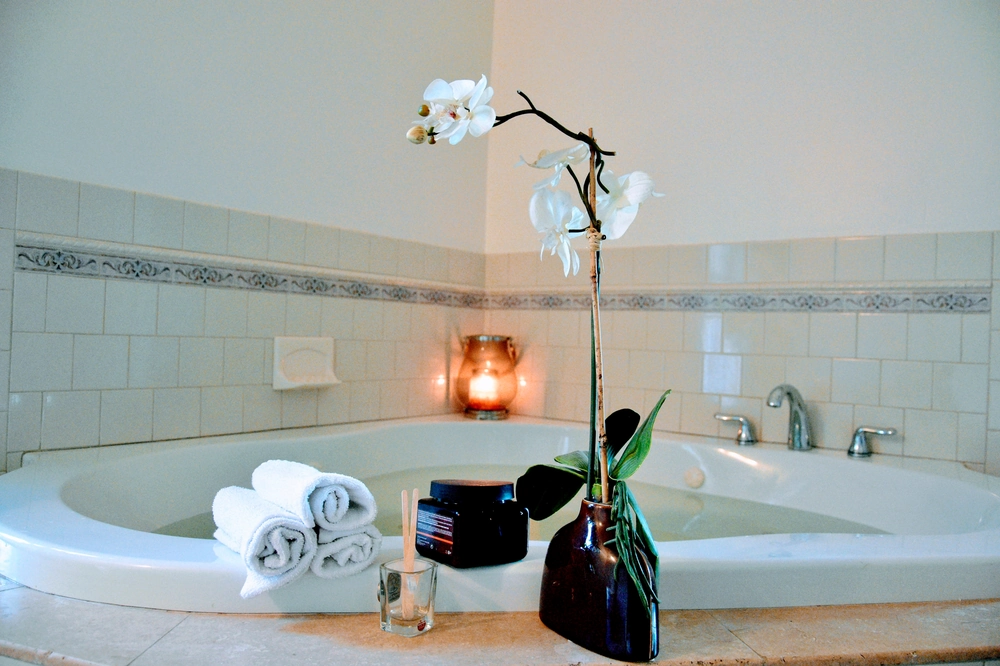 Aranżacja łazienki z narożną wanną, zwiniętymi ręcznikami, donicą z orchideą, świecą i eleganckimi akcesoriami spa