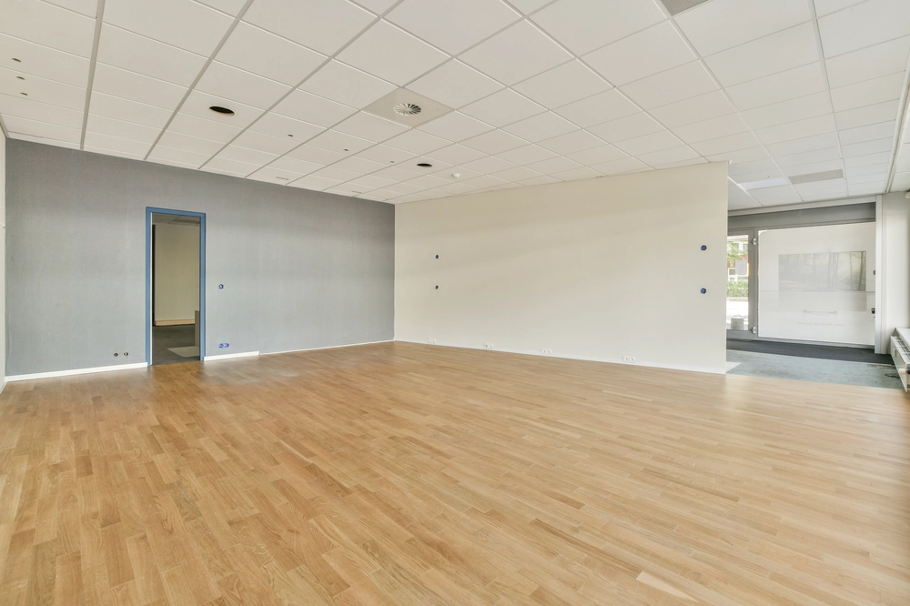 Przestronne puste wnętrze lokalu z nową drewnianą podłogą i podwieszanym sufitem