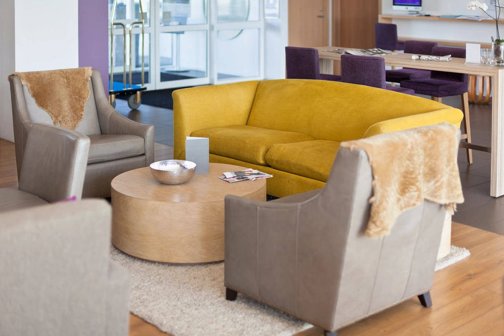 Nowoczesny salon firmowy z żółtą kanapą i szarymi fotelami przy drewnianym stoliku – wykończenie lokalu usługowego