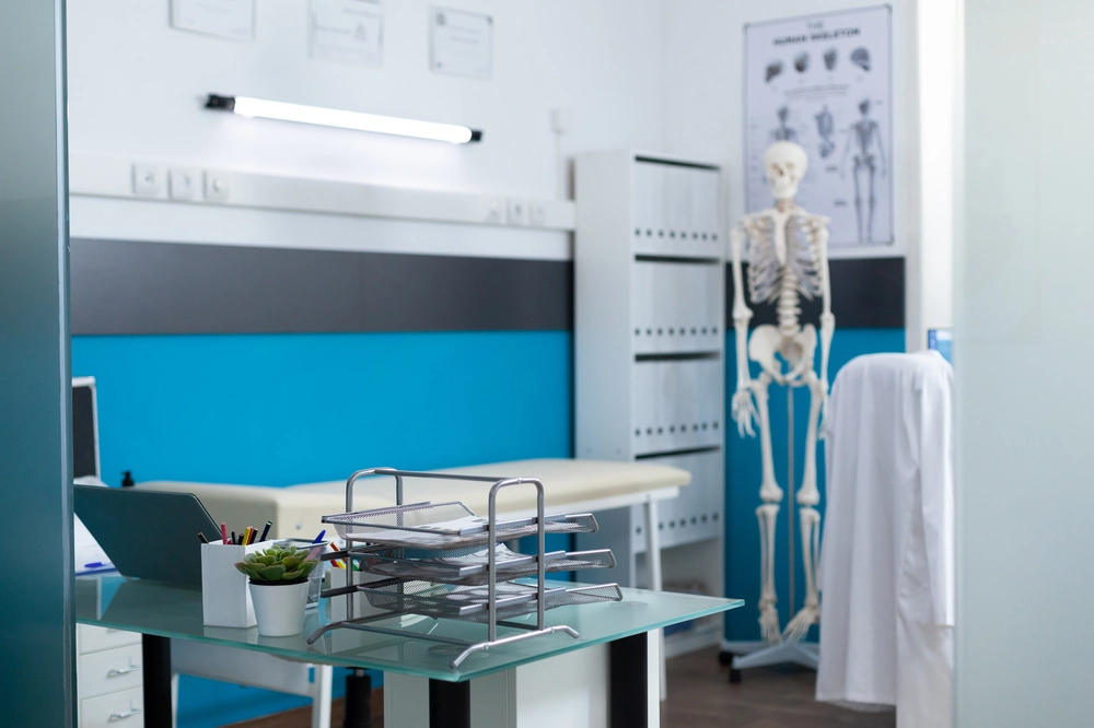 Nowoczesny gabinet medyczny z biurkiem, leżanką, modelem szkieletu i segregatorami