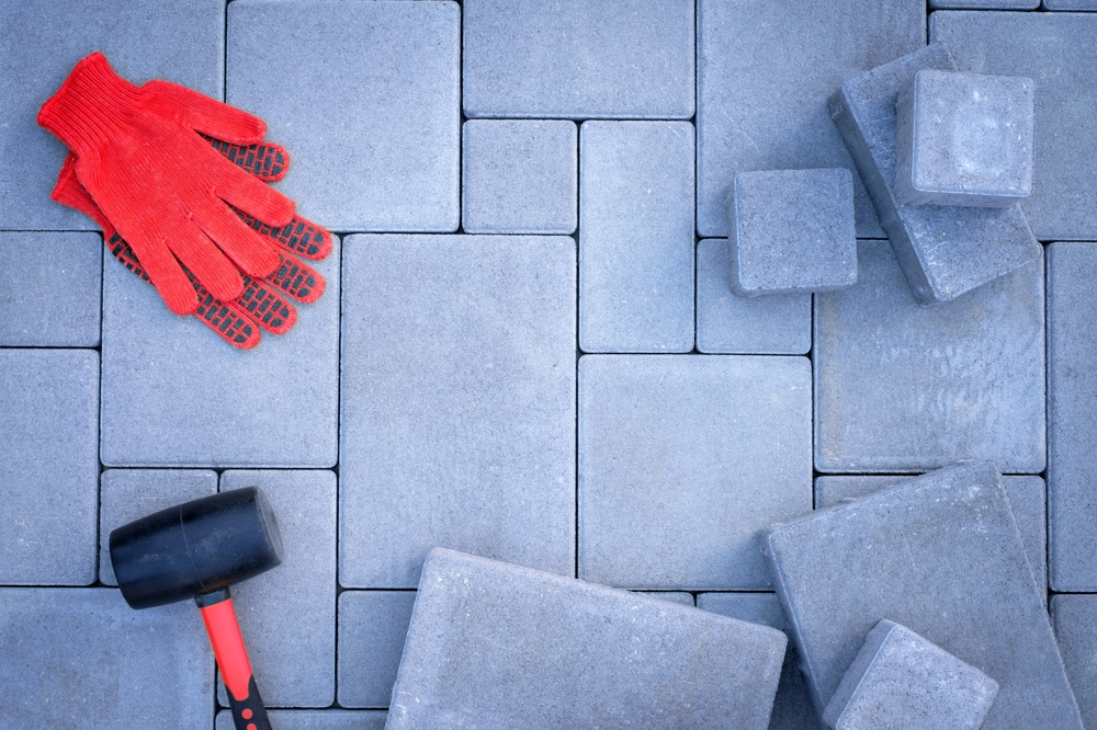 Kostka brukowa, układanie z czerwonymi rękawicami i gumowym młotkiem na szarej nawierzchni