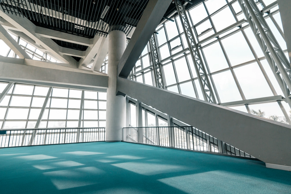 Jasne, przestronne wnętrze komercyjne z dużymi oknami i turkusową wykładziną dywanową