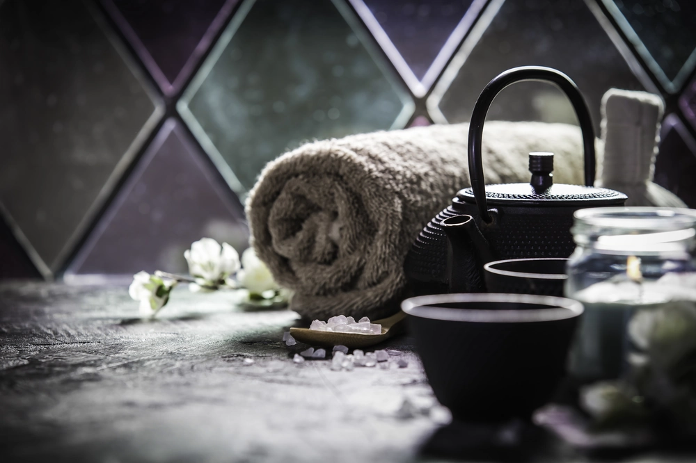 Detal wykończenia stref spa: rulon szarego ręcznika, żeliwny czajnik, miseczki z solą i zapalona świeca